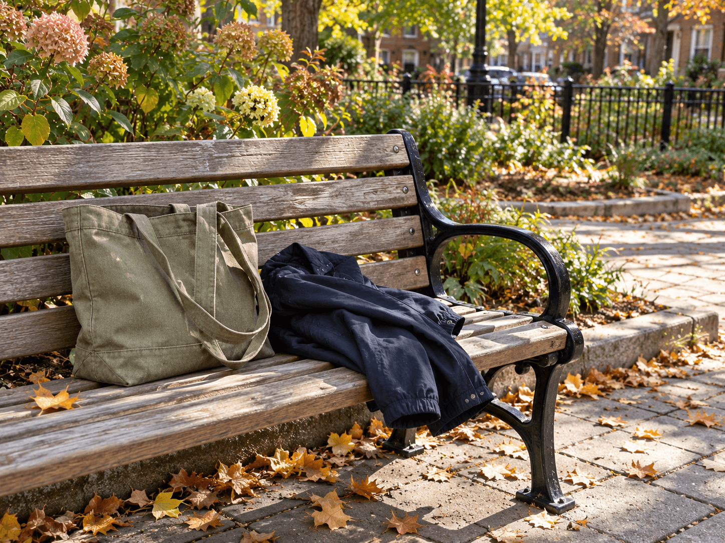 An ordinary public bench beside a small planted square, with Bea's canvas bag resting beside Luis's jacket.