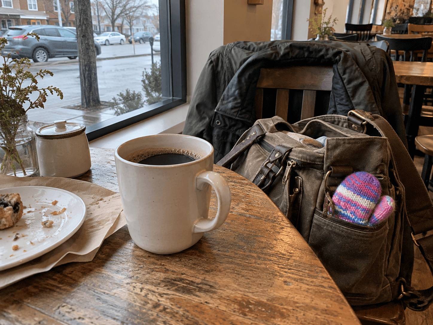 A coffee cup beside a parent's bag at a cafe table.