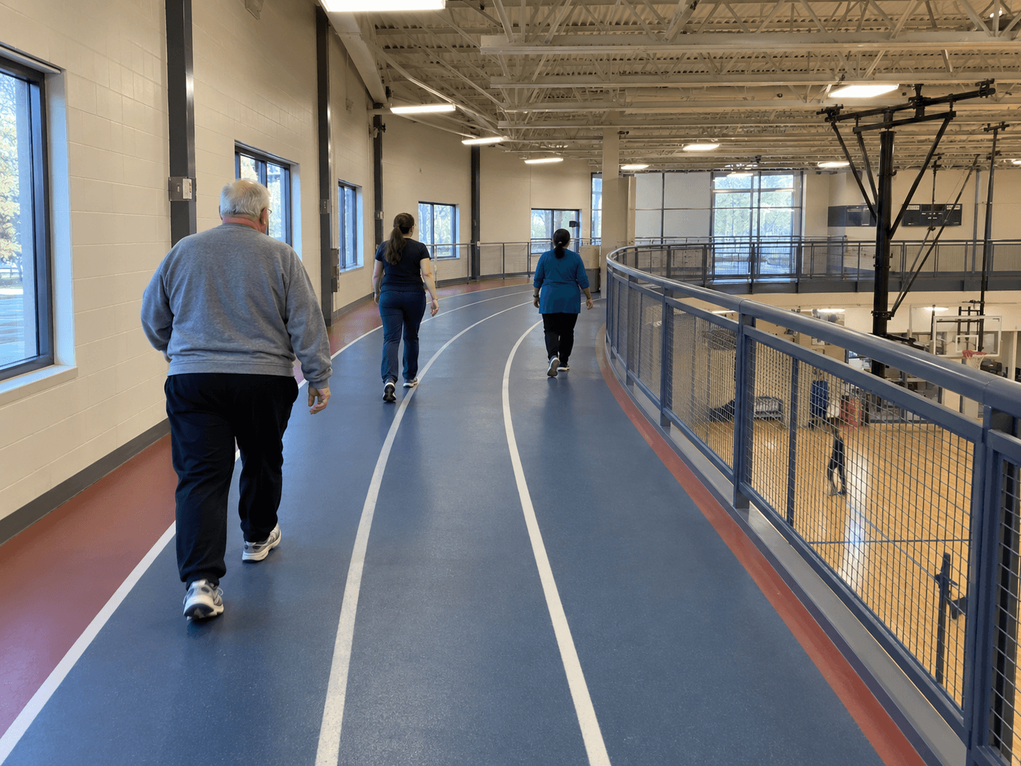 Adults walking at an ordinary pace along an indoor recreation-centre track, with clear lane markings and a solid railing.