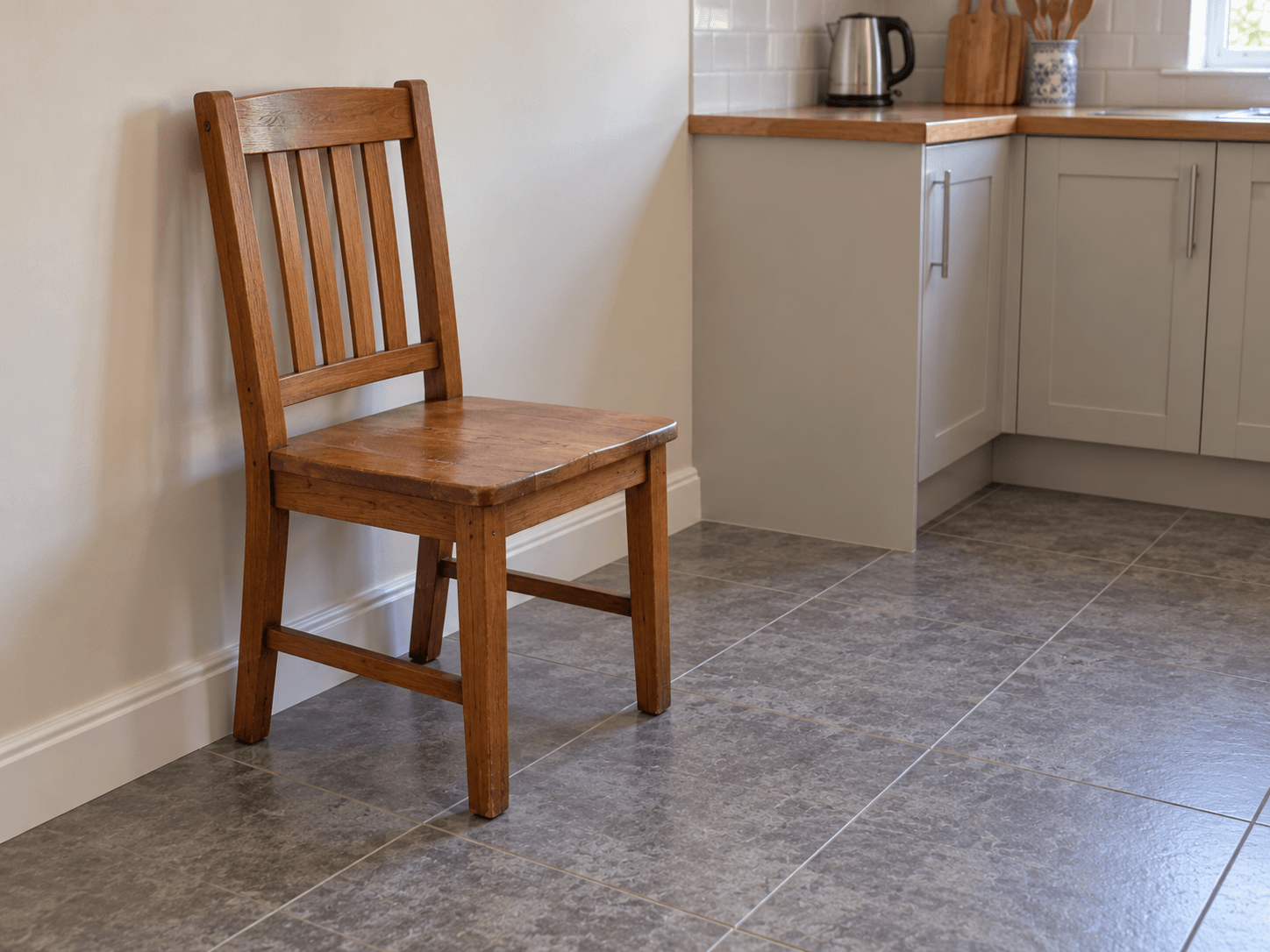 A heavy four-legged dining chair backed against a wall on a clear floor, away from a loose rug and trailing cables.