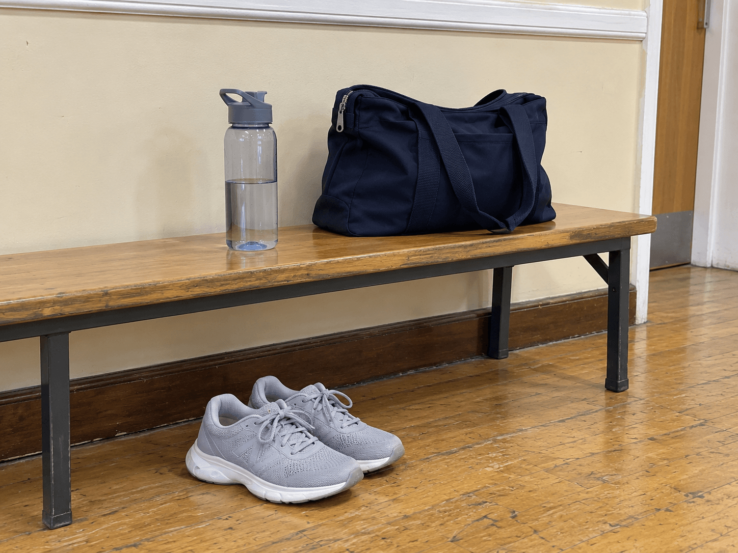 Comfortable trainers and a water bottle beside a zipped tote on a community-room bench after class.