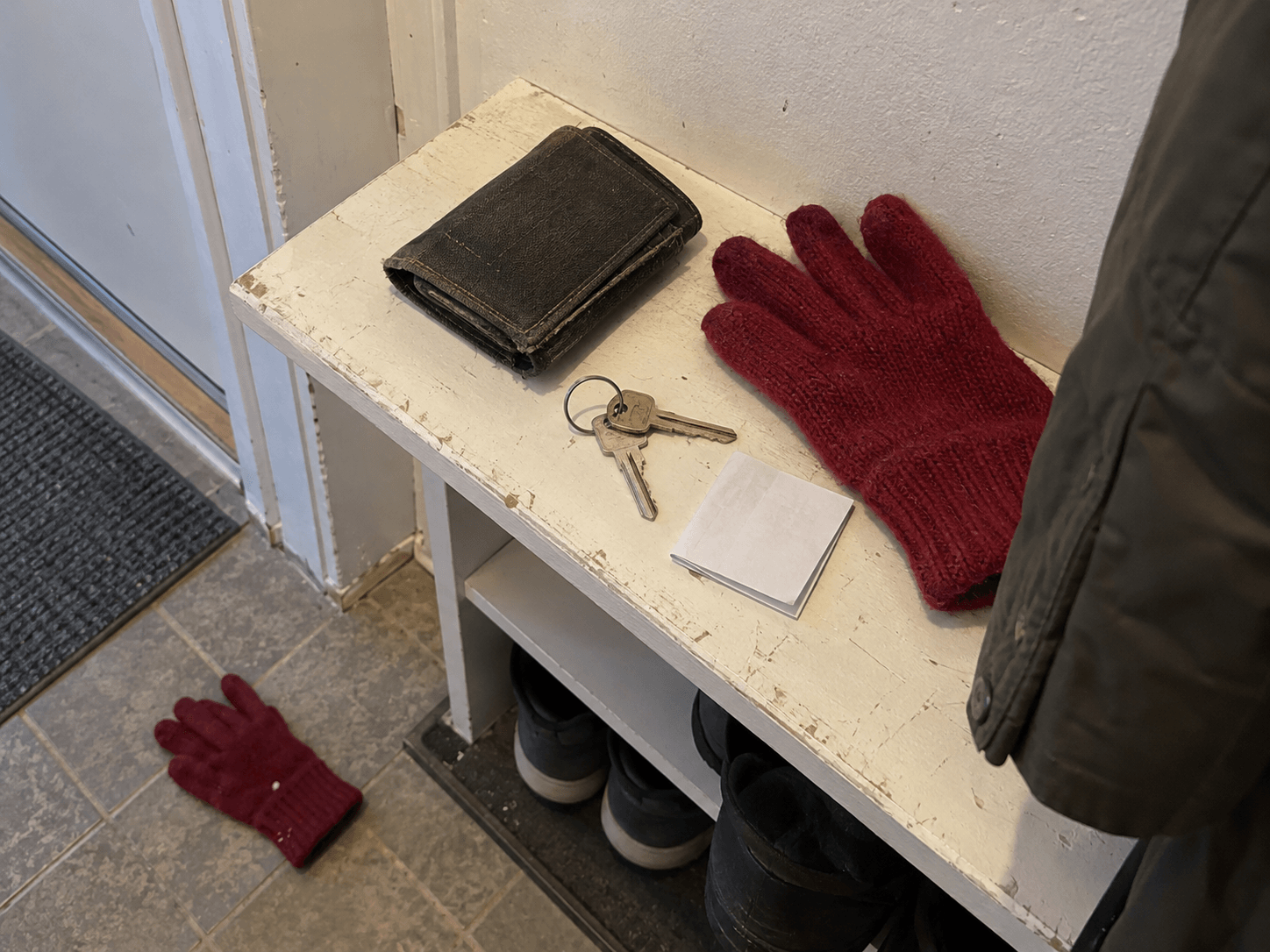 Keys and a folded note beside gloves at a front door.