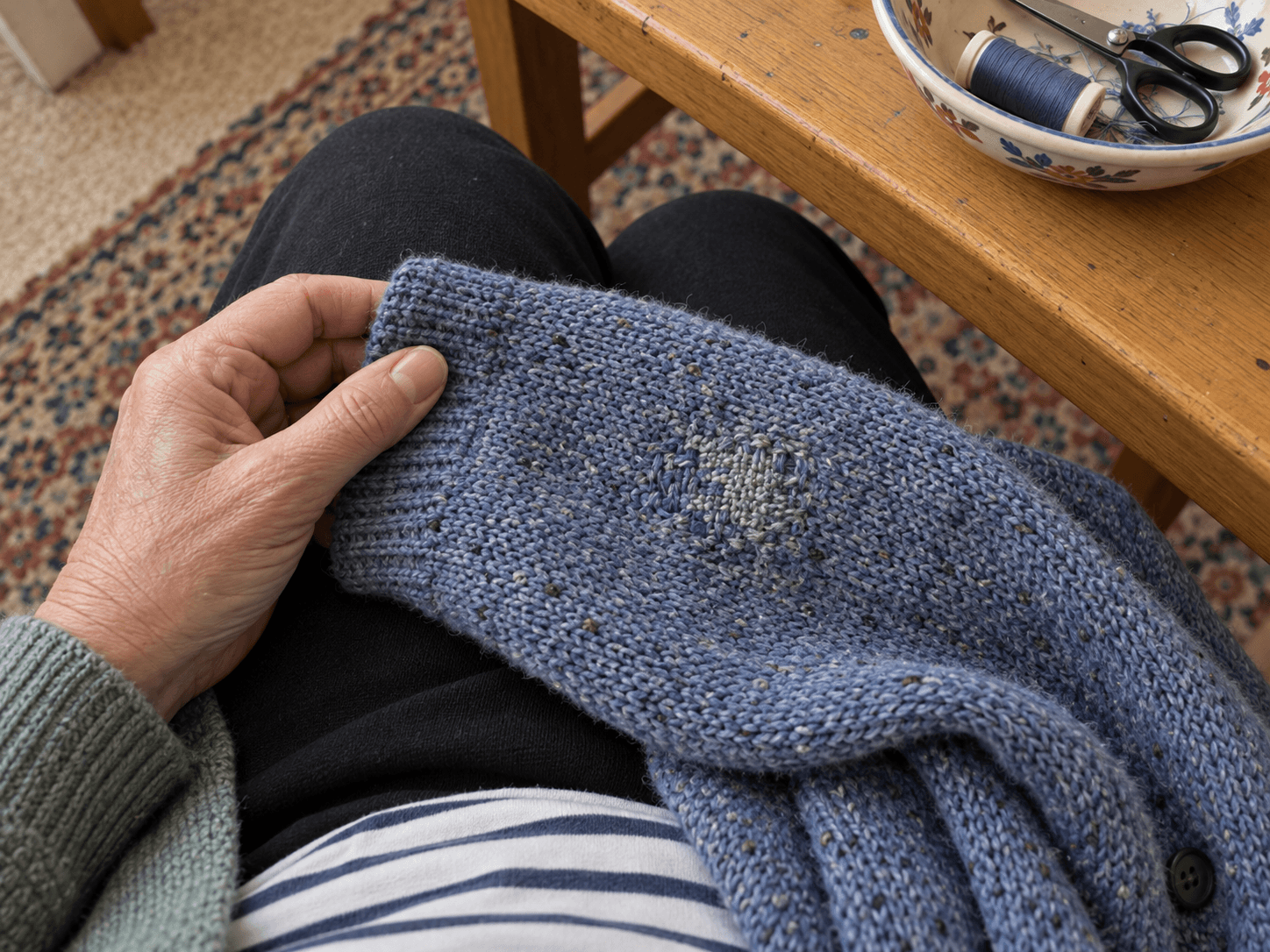 A visibly hand-mended blue cardigan sleeve on Harriet's lap, with a small sewing dish on the table nearby.