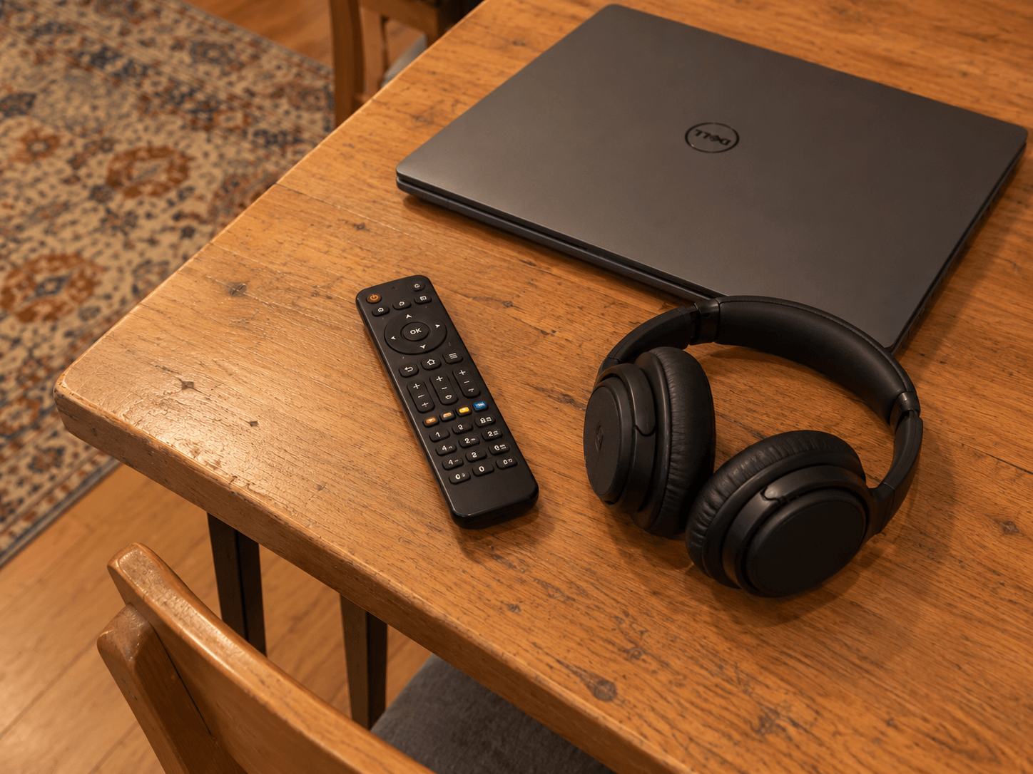 A television remote and a pair of over-ear headphones resting on a side table beside an ordinary sofa.