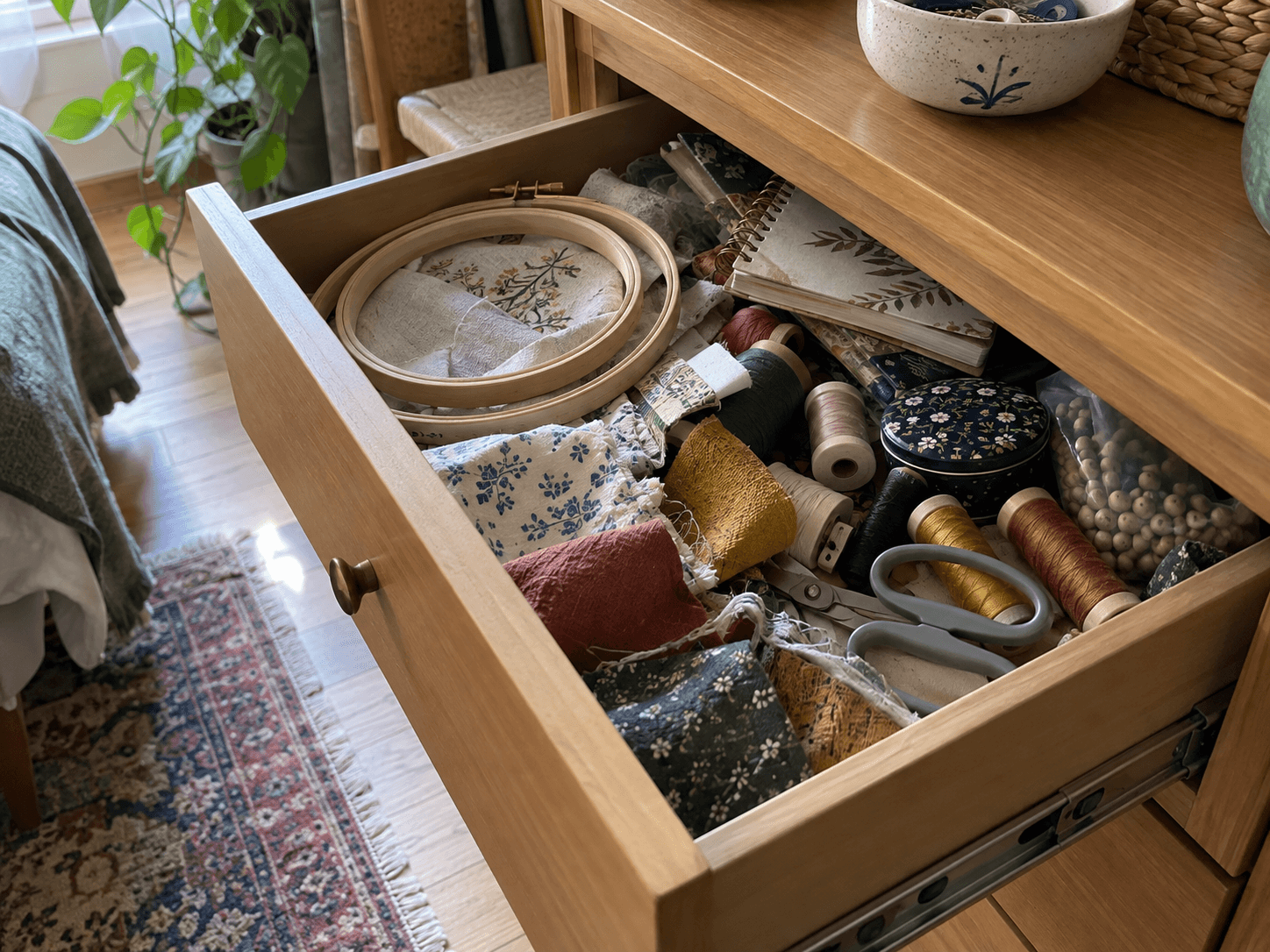 An open drawer of mixed craft supplies, with fabric offcuts, thread and a half-used notebook in an ordinary home.