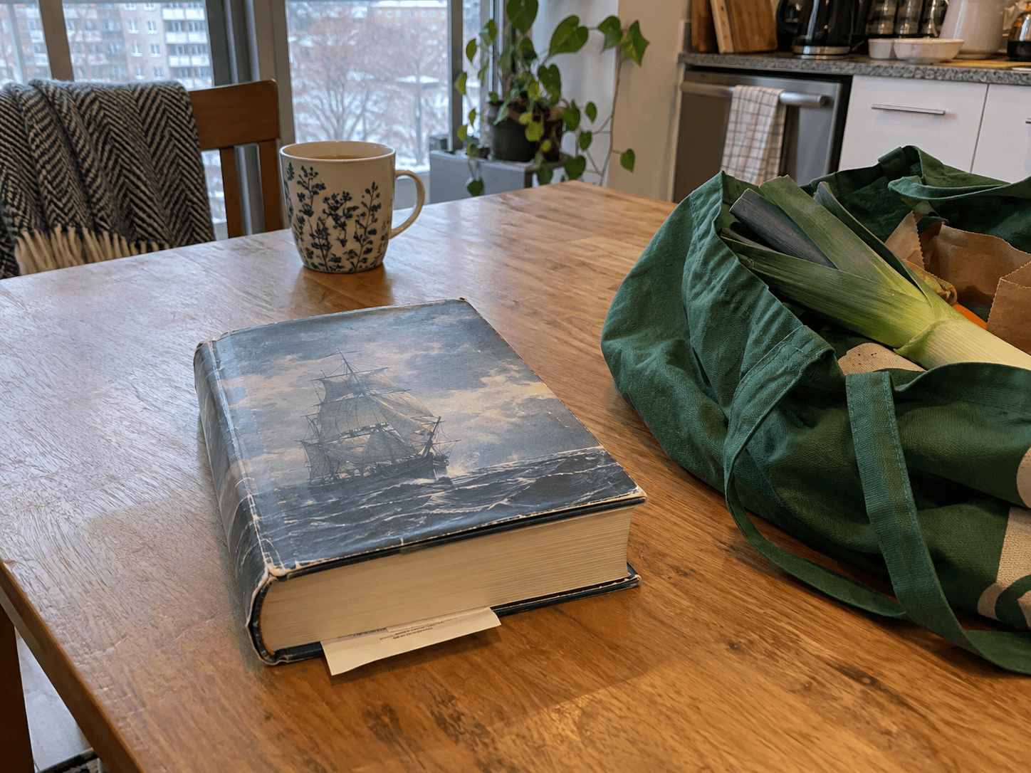 A library book with a slip tucked between its pages beside Ruth's shopping bag on a kitchen table.