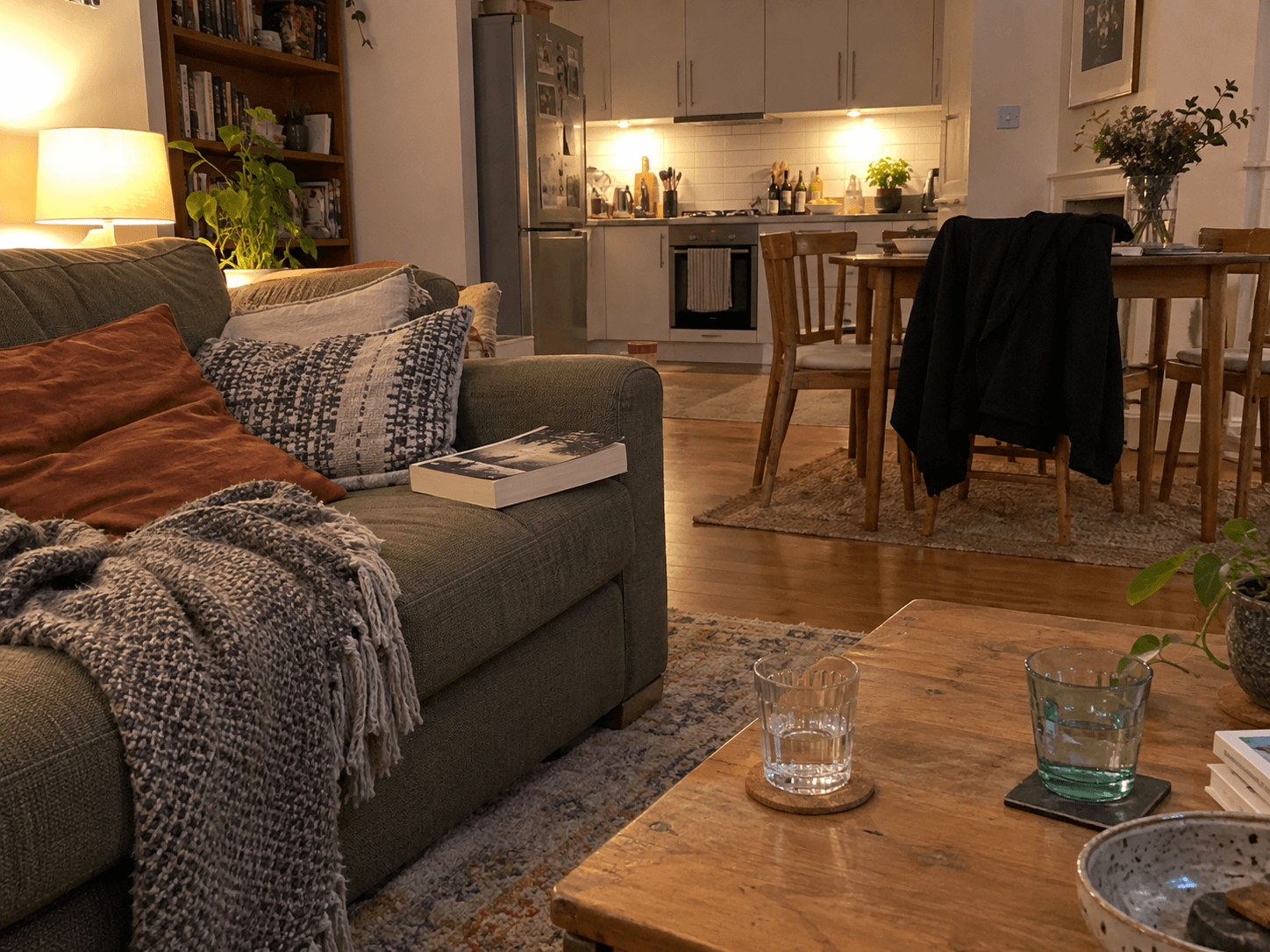 A paperback on a sofa seat, a jacket on a dining chair and two water glasses.