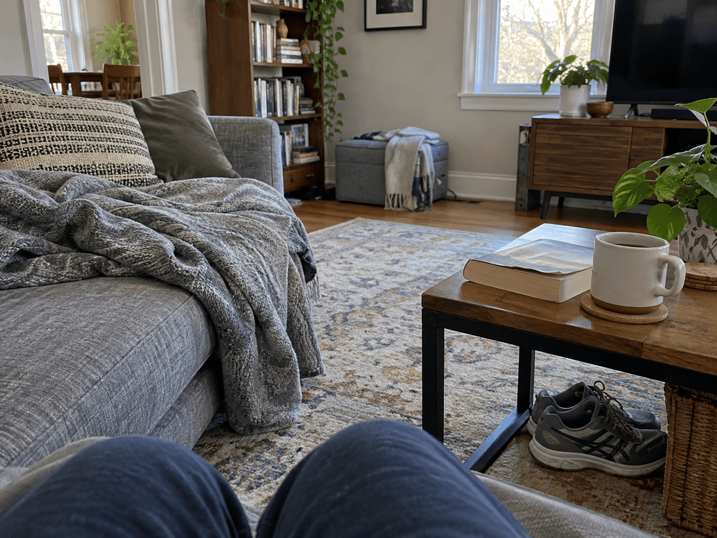 A sofa, blanket and book with running shoes tucked under the table.