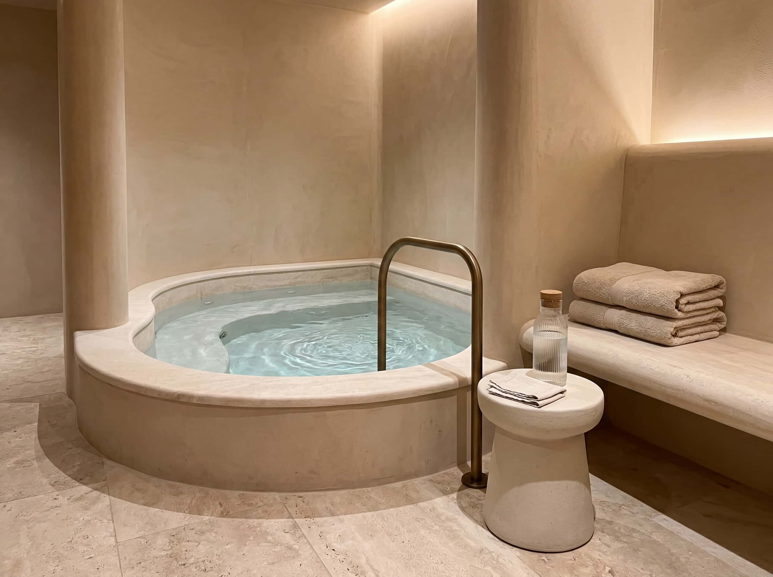 Cold plunge basin with brushed bronze rail and travertine stone bench